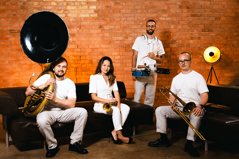 The band in white by a brick wall